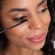Eine Frau trägt Mascara auf ihr Auge auf und präsentiert den Prozess des Auftragens von Make-up in einer hellen und eleganten Umgebung.